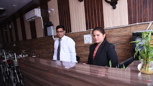 A reception desk with a wooden finish, a potted plant, and a wall-mounted air conditioner. - HBC Hotel Accurate (Rishikesh)