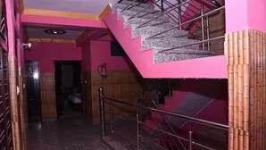 A staircase with metal railings leading to a room with pink walls and a wooden door. - HBC Hotel Accurate (Rishikesh)