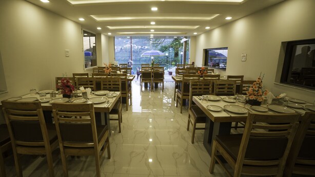 A dining area with multiple tables and chairs, a marble floor, and a view through the windows. - HBC Hotel Accurate (Rishikesh)