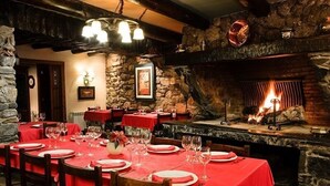 Ein Restaurant mit Steinwänden, einem Kamin und Tischen, die mit roten Tischdecken und Weingläsern gedeckt sind.