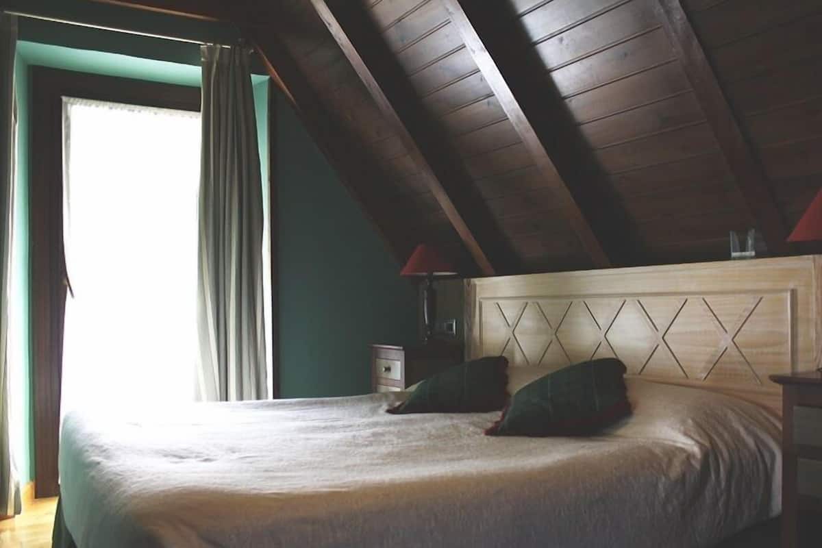Un dormitorio con techo de madera, una cama con cabecera, dos almohadas, una mesita de noche y una lámpara.