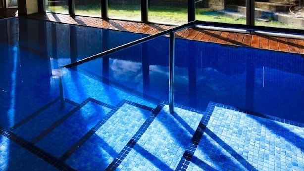 Ein Innenpool mit klarem, blauem Wasser, Holzstufen und Blick auf Grünflächen.