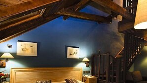 Ein Schlafzimmer mit geneigter Decke, Holzbalken, einem Bett mit gestreiften Kissen, zwei Wandlampen und gerahmten Bildern.