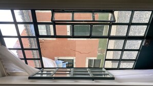 Una habitación con un ventanal de diseño enrejado, una cortina blanca y vistas a un edificio vecino de fachada roja.