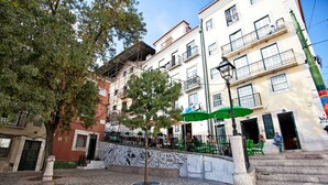 Una plaza adoquinada con un árbol, una escalera y edificios con balcones.