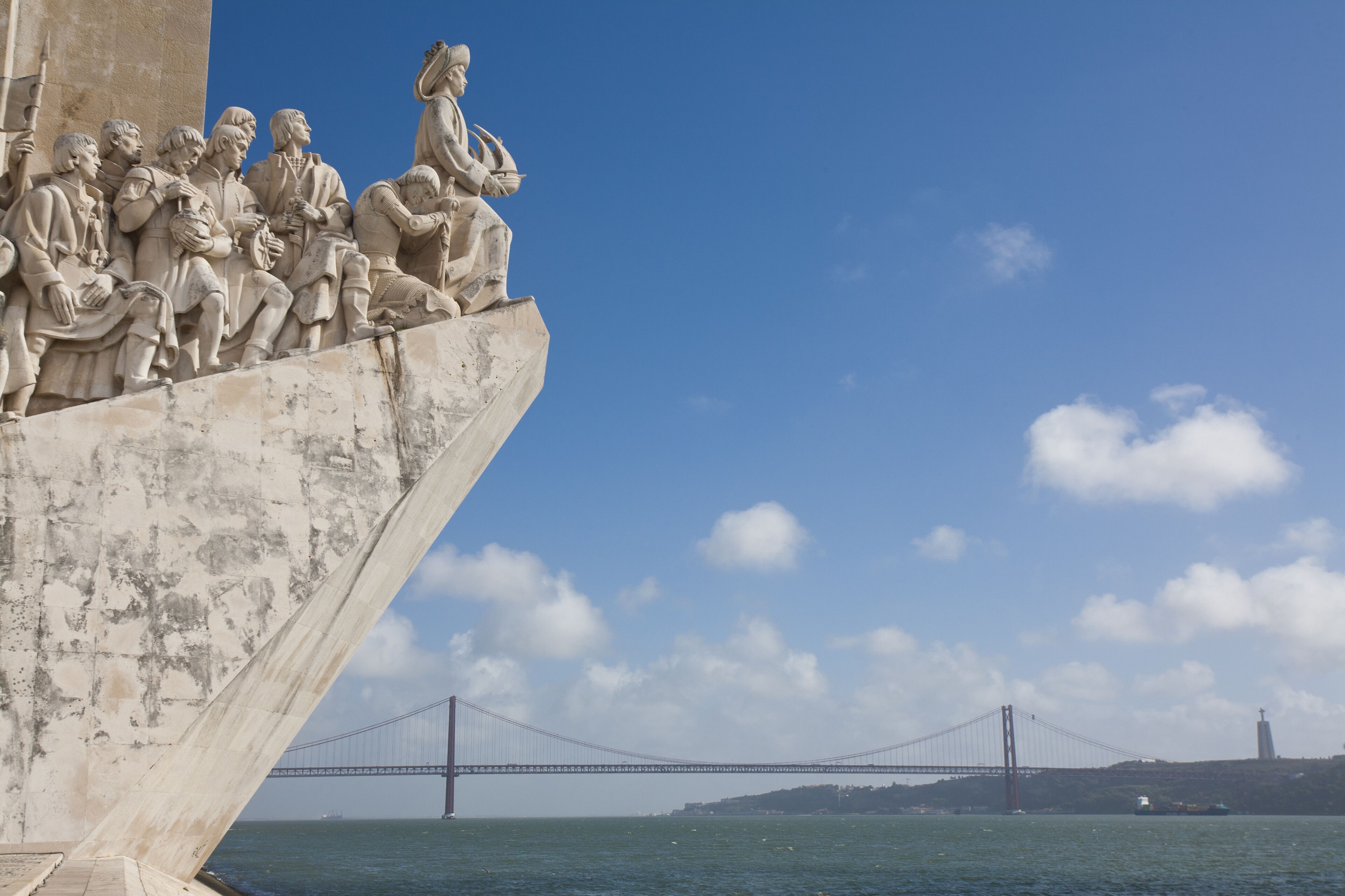 A bridge with a statue of people on a cliff overlooking the water.