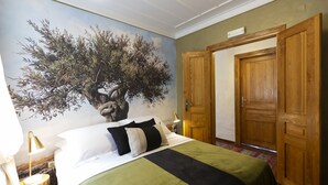 Una camera da letto con un letto, un comodino, una lampada, una porta in legno e un affresco sul muro.