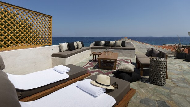 Zona relax all'aperto illuminata dal sole con vista sul mare, completa di poltrone prendisole, un tavolino e un recinto decorativo.