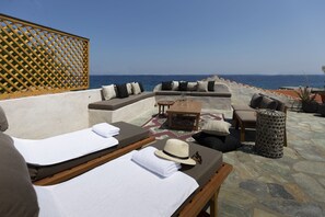 A sunlit outdoor seating area with a view of the sea, featuring lounge chairs, a small table, and a decorative fence. - Villa of the old olive oil factory (Samos)