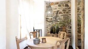 Zona pranzo con un tavolo rotondo in legno, sedie, una lampada a sospensione e un muro in pietra.