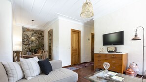 Un soggiorno con un divano, un tavolino in vetro, una televisione, un muro in pietra, porte in legno e una lampada.