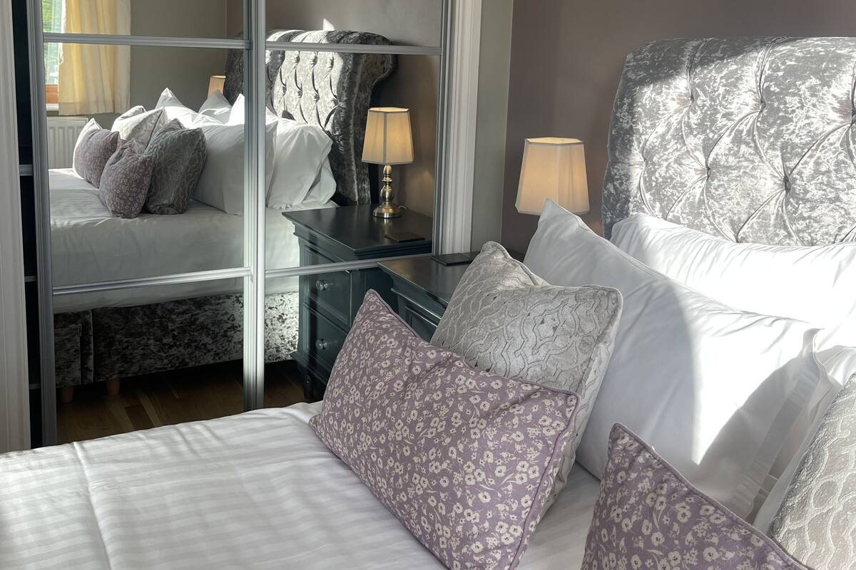 A bedroom with a large bed, a nightstand, a lamp, and a mirror.