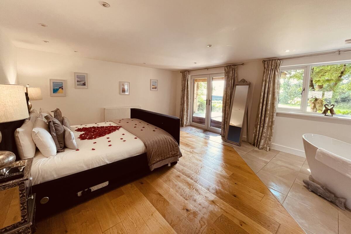 A spacious bedroom with a large bed, a sitting area with a table and chairs, and a view of the outdoors through a sliding glass door.