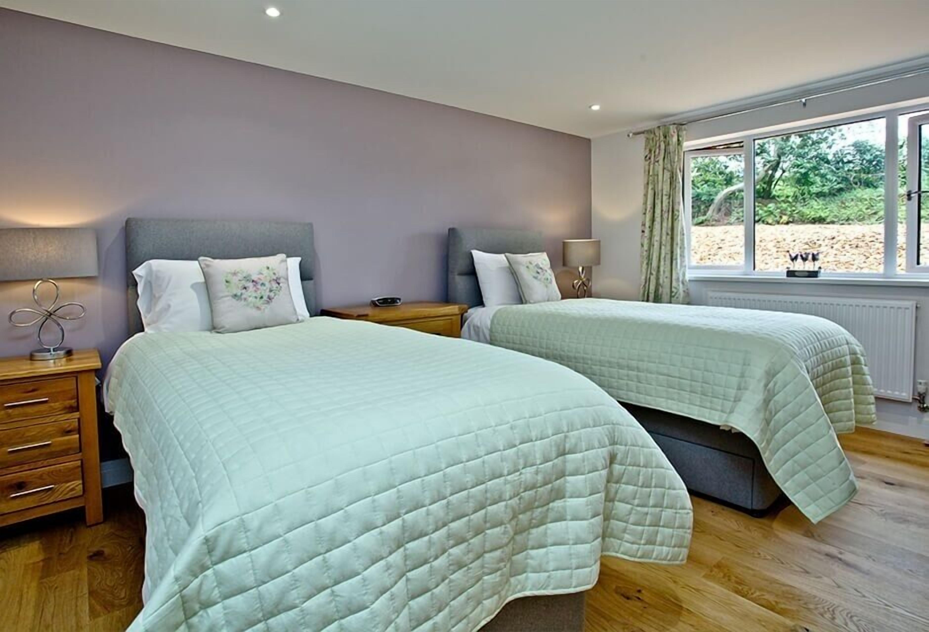 A bedroom with two beds, wooden flooring, and a window with a view of greenery.