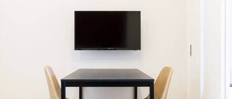A room with a black TV mounted on the wall, a black table, and two brown chairs.