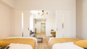 A hotel room with two beds, a small table, a sofa, and a desk with a chair. There is a hallway leading to another room and a door at the end. - SG Residence Inn Hakata (Fukuoka)