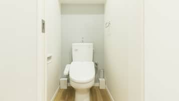 A small, white bathroom with a toilet, a shelf above the toilet, and a wooden floor.