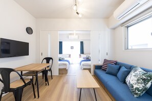 A modern room with a wooden table, two chairs, a sofa with blue cushions, a flat-screen TV, and a ceiling light fixture. - SG Residence Inn Hakata (Fukuoka)