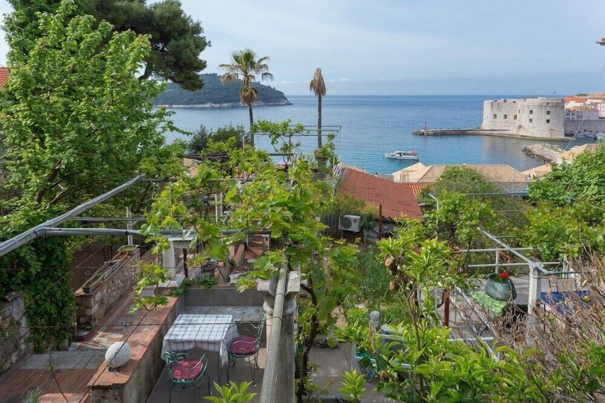 Une terrasse avec une table et des chaises, donnant sur une zone côtière où se trouve un bâtiment historique et, au loin, une petite île.