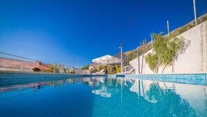 Ein klarer, blauer Swimmingpool mit Fliesenrand, umgeben von einer Betonmauer und einem Gebäude mit einem Ziegeldach.