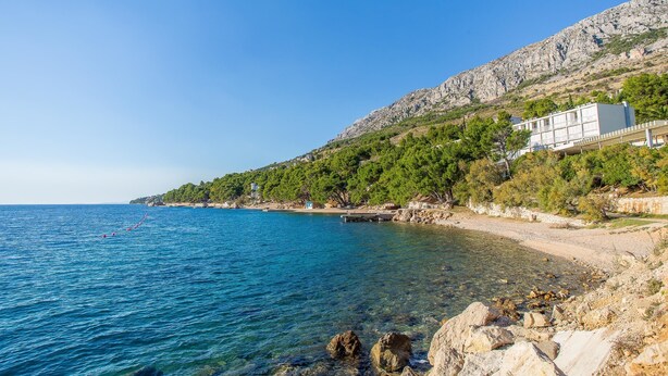 Ein Küstenhotel mit freiem Blick auf das Meer, einer felsigen Küstenlinie und einer bergigen Landschaft im Hintergrund.