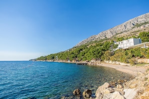 A coastal hotel with a clear view of the sea, a rocky shoreline, and a mountainous backdrop. - Apartments Emil Zora (Omis)