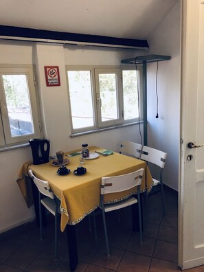 A dining area with a table set for two, two chairs, a window with a view, and a no-smoking sign on the wall. - Domus Santa Caterina (Rome)