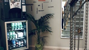 A vending machine with a coffee dispenser, a potted plant, and a wall with a 'Welcome' sign surrounded by various words. - Domus Santa Caterina (Rome)