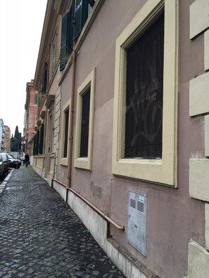 A narrow cobblestone street with buildings featuring large windows and a visible gas meter. - Domus Santa Caterina (Rome)