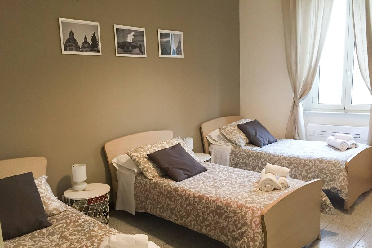A hotel room with two beds, a small round table, a chair, and three framed pictures on the wall.