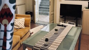 A living room with a glass-top dining table, a sofa, a TV, and a staircase leading to another level. - Domus Santa Caterina (Rome)