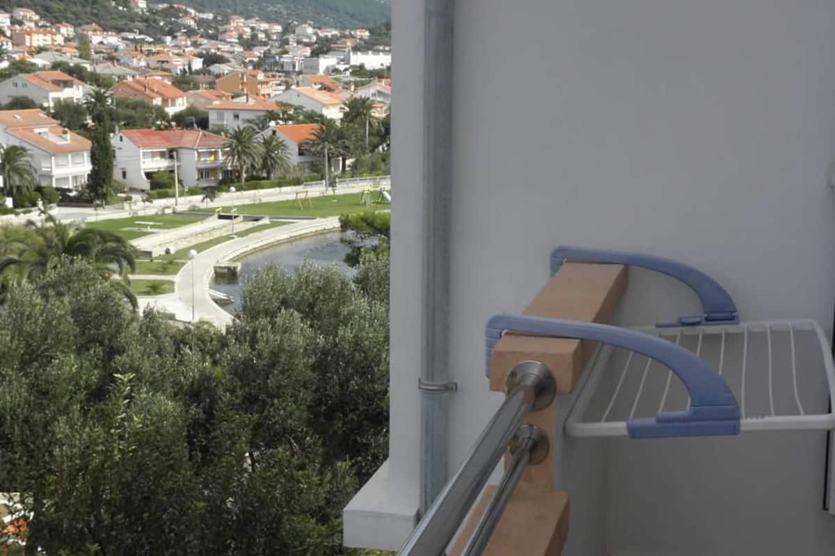 Uma varanda com vista para uma área residencial, um espelho d'água e guarda-corpo de metal.
