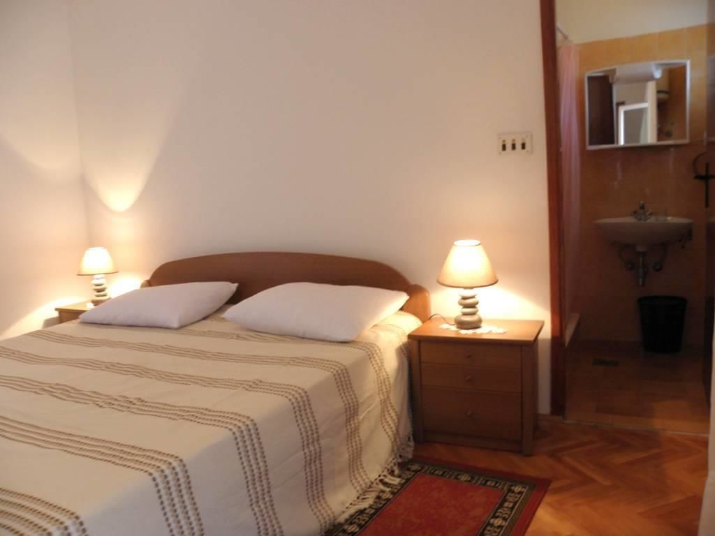 Un lit bien fait, recouvert d’une couvre-lit à rayures et agrémenté de deux oreillers, avec deux tables de chevet surmontées de lampes. On aperçoit un petit tapis sur le sol.