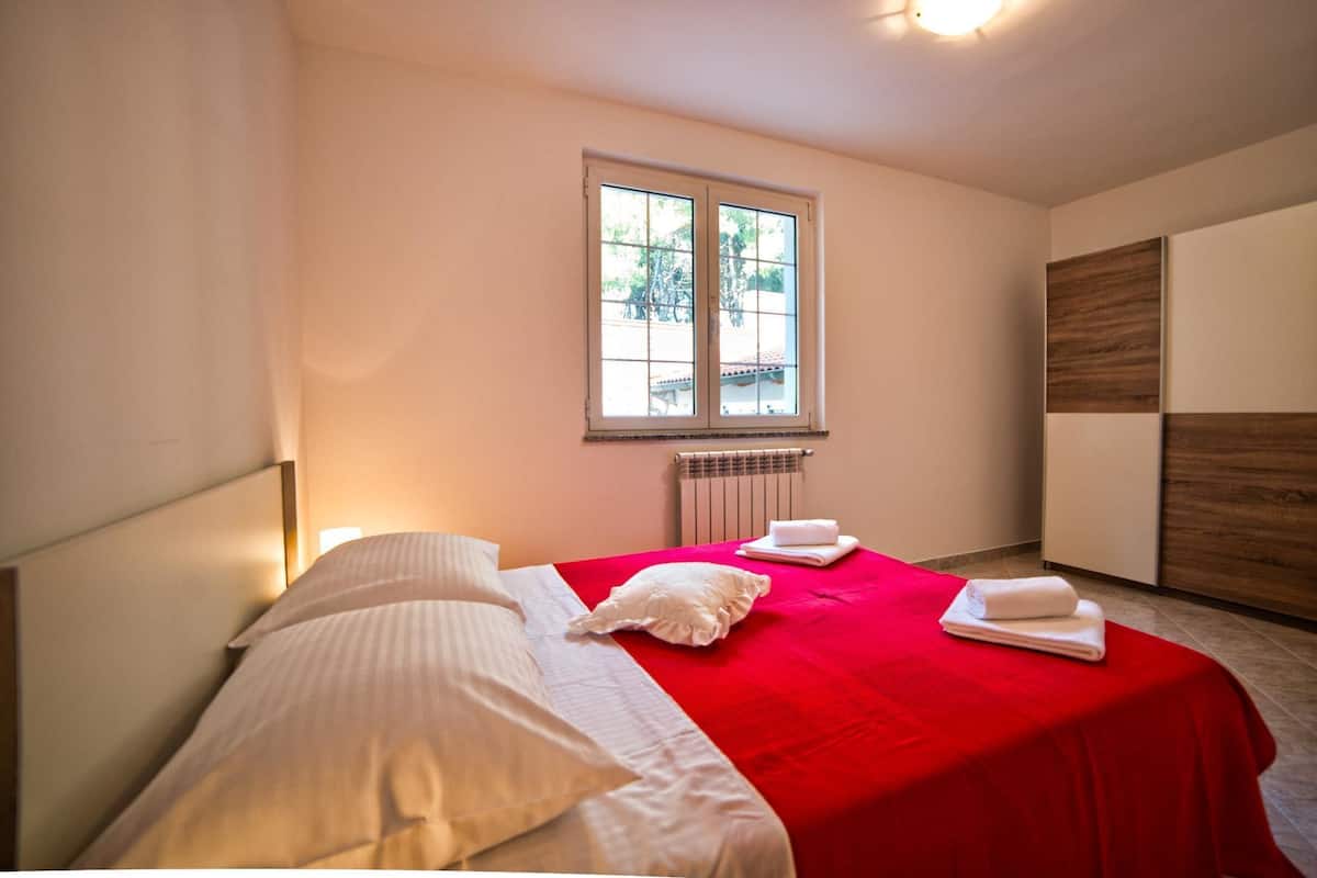 A hotel room with a bed, a window, a radiator, and a wooden wardrobe.