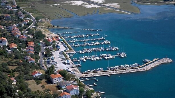 An aerial view of a coastal marina with numerous boats docked, surrounded by residential buildings and a small pier. - Apartments Vesna Sup.draga (Rab)