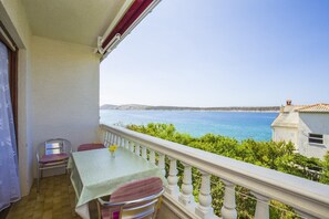 Een balkon met een tafel en stoelen, met uitzicht op de kust en een gebouw op de achtergrond.