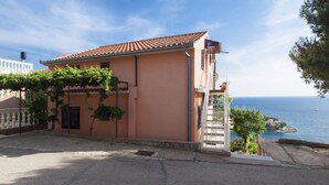 A two-story building with a tiled roof, a balcony with a white railing, and a view of the sea. - Apartments Nikica Primosten (Primosten)