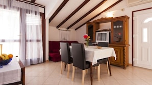 A dining area with a table set for two, a red sofa, and a wooden cabinet with a television. - Apartments Nikica Primosten (Primosten)