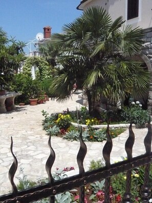 A courtyard with a stone floor, potted plants, and a metal fence. - House Percan Zora (Marcana)
