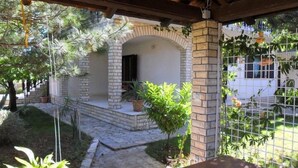A covered patio area with a brick archway, potted plants, and a view of a white building through a wire fence. - Apartments Carev (Tisno)