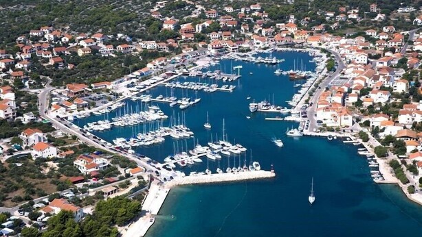 An aerial view of a coastal town with a marina filled with boats, surrounded by residential buildings with red roofs. - Apartments Carev (Tisno)