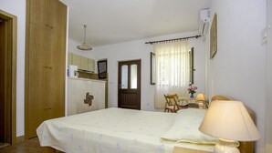 Ein Schlafzimmer mit einem Bett, einem Holzschrank, einem kleinen Tisch mit Lampe, einem Stuhl, einem Fenster mit Vorhängen und einer Tür.
