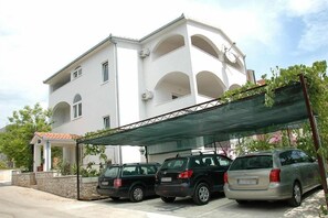A white building with multiple balconies and a covered parking area with two cars. - Apartments Lukić (Okrug)