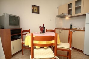 A compact kitchen with a dining table, chairs, a television, and basic appliances. - Apartments Lukić (Okrug)