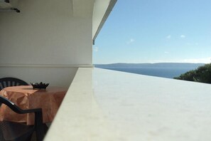 A balcony with a table and chairs, overlooking a scenic view of the sea and distant hills. - Apartments Lukić (Okrug)