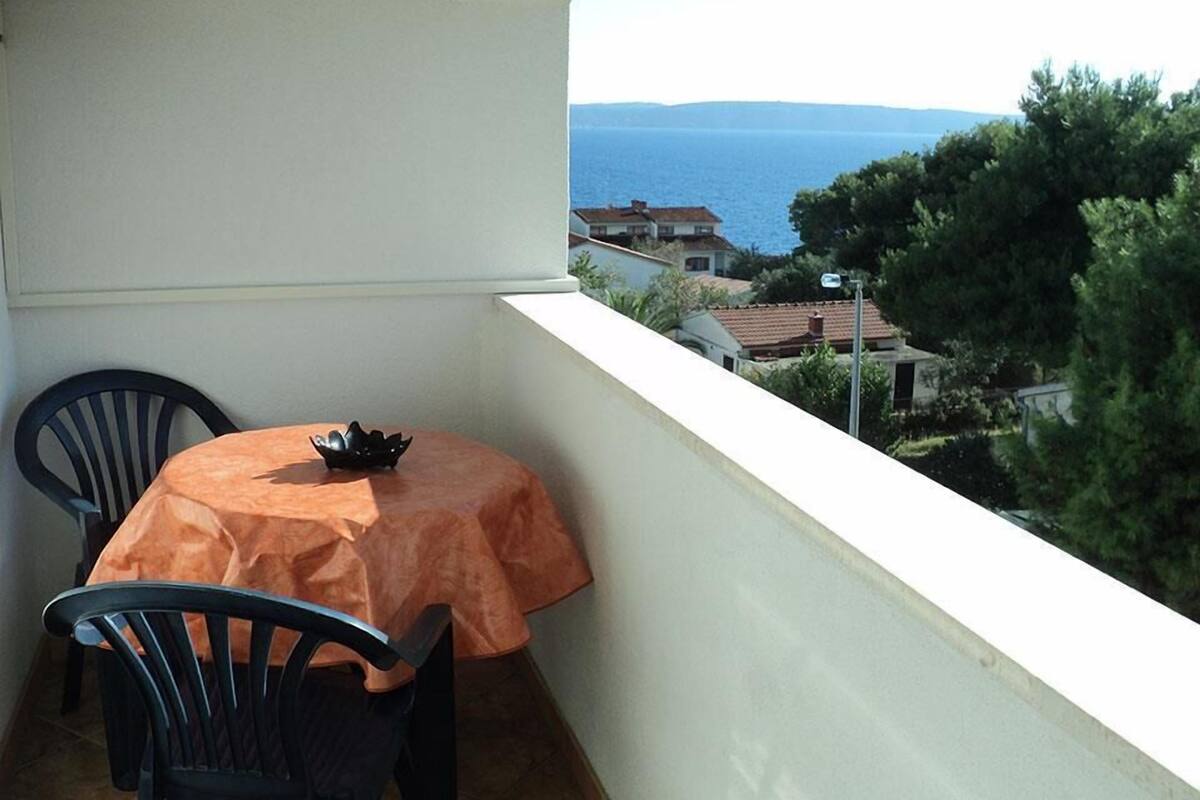 A balcony with a table and chairs, overlooking a coastal view with houses and trees.