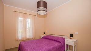 A bedroom with a bed, two bedside tables, a nightstand, a lamp, and a window with curtains. - Apartments Zazah (Liznjan)