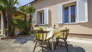 An outdoor seating area with a table and chairs, a palm tree, and a building with shutters. - Apartments Zazah (Liznjan)