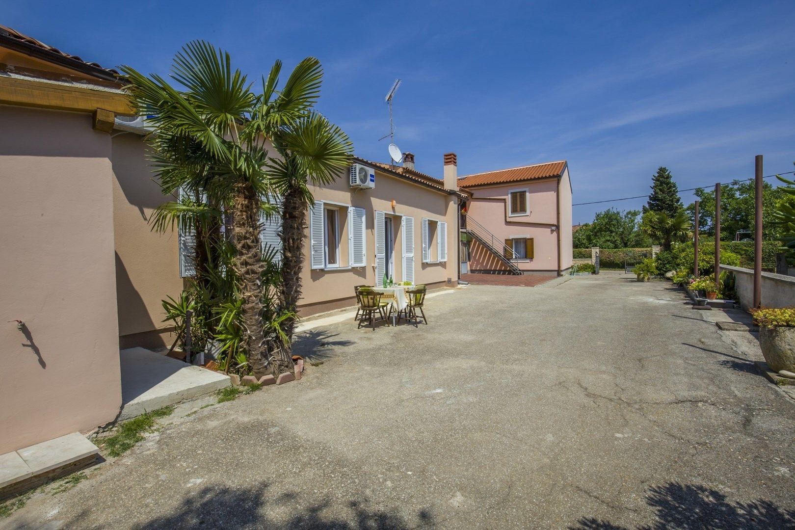 A residential area with a paved driveway, a palm tree, and a small table with chairs.