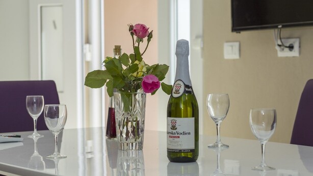 A table with a bottle of wine, a vase with flowers, and empty wine glasses. - Apartments Zazah (Liznjan)